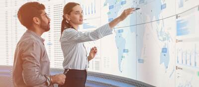 GettyImages-1522425942-two-coworkers-in-front-of-large-monitor-HEADER-2400x1600