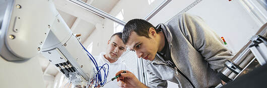 Two men work on robot.