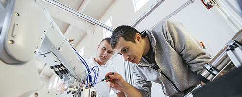 Two men work on robot.
